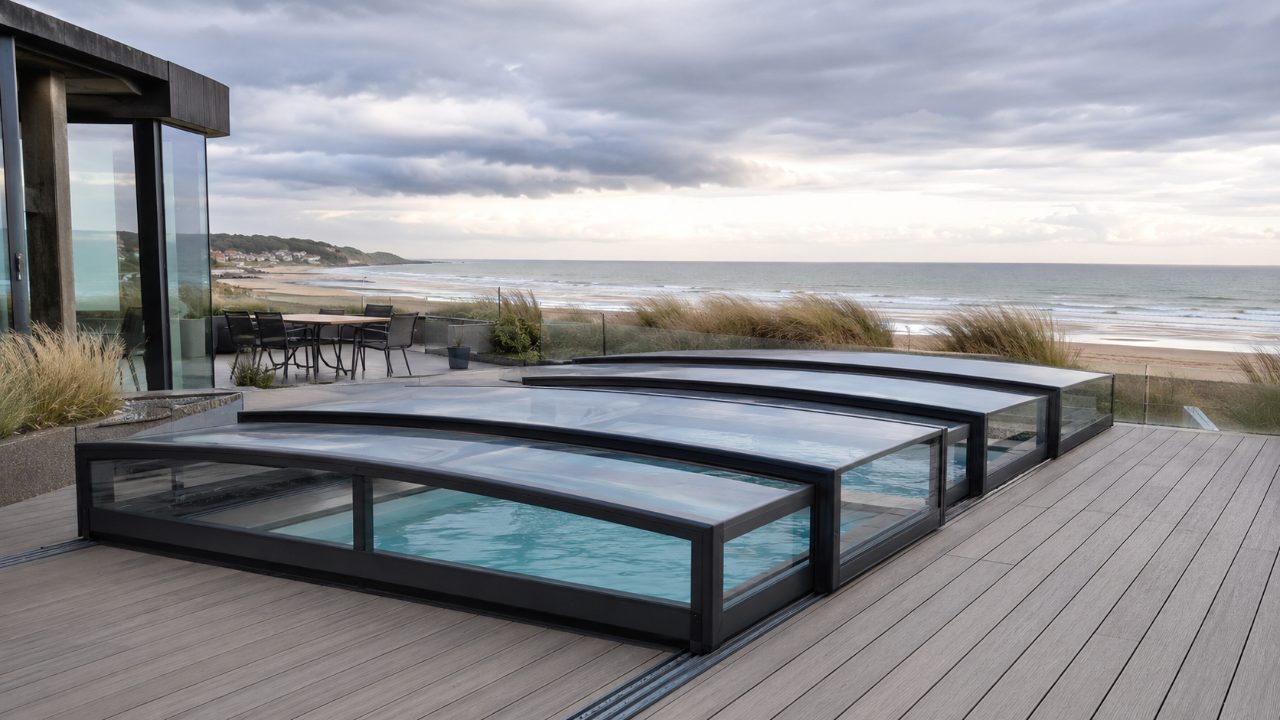 Abri de piscine télescopique en aluminium sur une terrasse en bord de mer de la Côte d'Opale, sous un ciel venteux.